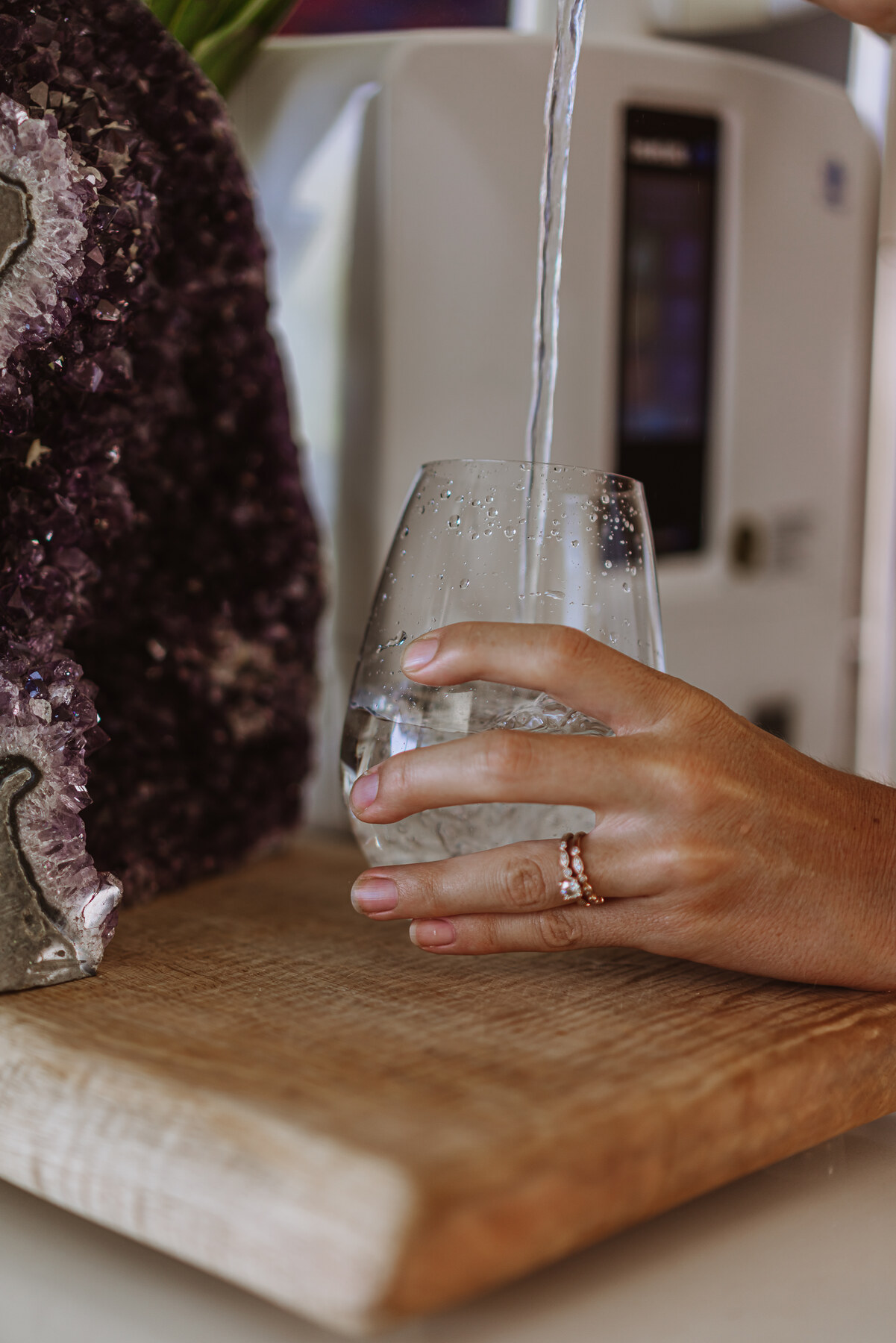 A hand holding a glass of Kangen Water beside an amethyst crystal